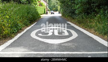 Primo piano di segnaletica stradale con limite di velocità di 30 km/h dipinta su strada rurale, campagna britannica. Contrassegni di riconoscimento della limitazione di velocità. Foto Stock