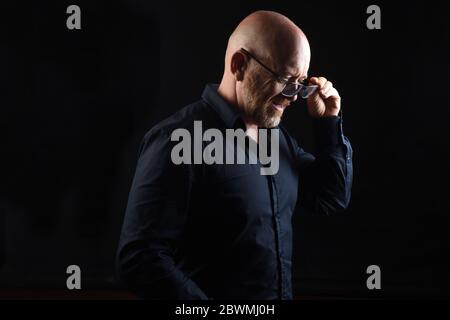 uomo che togli i suoi occhiali su sfondo nero Foto Stock