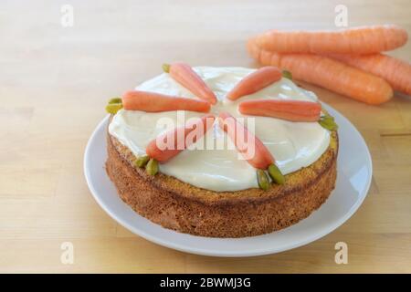 Torta di carote con glassatura e decorazione di marzapane e pistacchi, spesso cotti al forno durante le vacanze di Pasqua, tavolo in legno con spazio per la copia, selezionato morbido in foc Foto Stock