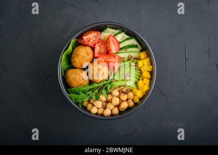 Ciotola di buddha vegetariana con cetriolo, avocado, falafel, pomodoro e ceci su sfondo nero, vista dall'alto Foto Stock