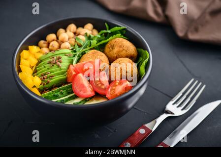 Ciotola di buddha vegetariana con cetriolo, avocado, falafel, pomodoro e ceci su sfondo nero Foto Stock