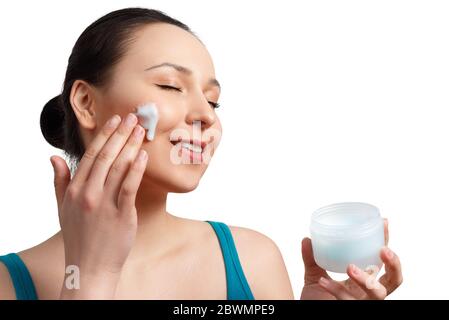 Felice sorridente bella donna che applica crema idratante sul viso. Isolato su sfondo bianco. Foto Stock