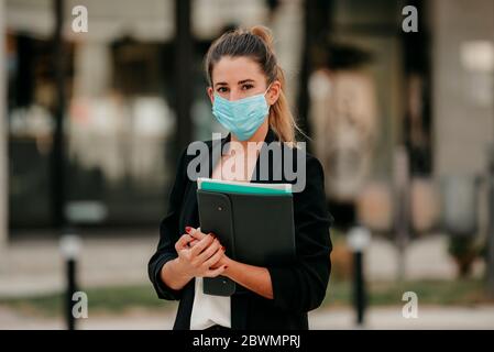 giovane donna d'affari che va a lavorare giù la strada indossando maschera medica Foto Stock