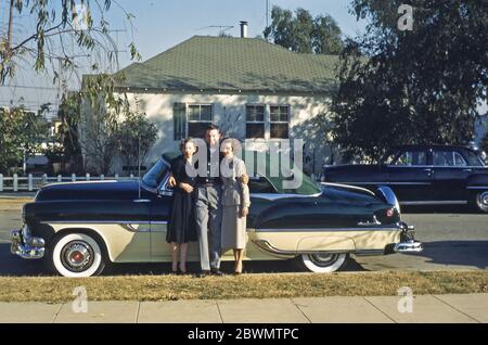 Un uomo mostra il suo orgoglio e la sua gioia, una Pontiac Star Chief soft-top auto USA c. 1955. Ha le braccia intorno a due donne che sono vestiti elegantemente, una più giovane e l'altra più anziana. Tra il 1954 e il 1957, il Capo Stella fu il modello di prestigio di Pontiac e fu basato sul Pontiac Chieftain. Foto Stock