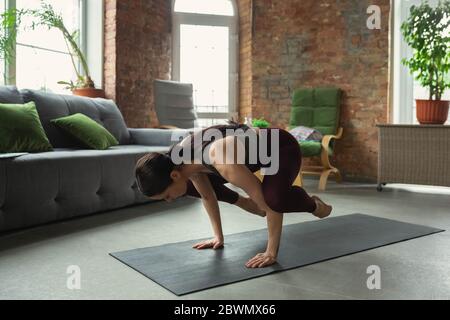 Forza. Sportivo bella giovane donna che pratica le asana di yoga come professionista a casa. Concetto di stile di vita sano, benessere, alla ricerca di un nuovo hobby. Flessibile e motivato. Foto Stock