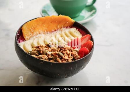 Recipiente per frullato con fragola, frutta drago, mango e mulo in ciotola di cocco e su tavolo bianco Foto Stock