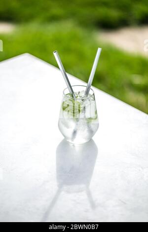 Bel bicchiere d'acqua o mojito con cocktail di lime e menta sullo sfondo verde e tavolo bianco atmosfera estiva Foto Stock