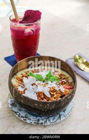 Recipiente per frullati con mango, yogurt, muesli e fragole in una ciotola di cocco su sfondo chiaro Foto Stock