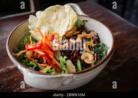 Riso Rosso biologico Nasi Goreng, riso vegetariano fritto con un sacco di verdure, tofu e cashews tostati in ciotola su sfondo di legno Foto Stock