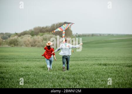 Felice coppia che si diverte insieme, giocando con kite sul green field. Coppia felice che si aspetta un bambino e un concetto di famiglia giovane Foto Stock