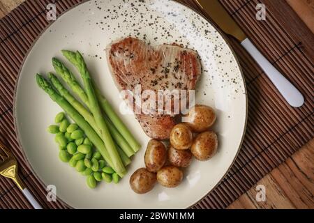 Bistecca di tonno alla griglia servita con asparagi, patate arrosto, fagioli di edamame e salsa hollandaise su un piatto, vista dall'alto Foto Stock