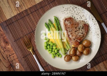 Bistecca di tonno alla griglia servita con asparagi, patate arrosto, fagioli di edamame e salsa hollandaise su un piatto, vista dall'alto Foto Stock