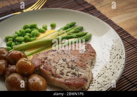 Bistecca di tonno alla griglia servita con asparagi, patate arrosto, fagioli di edamame e salsa hollandaise su un piatto, vista dall'alto Foto Stock