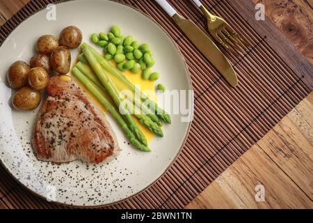 Bistecca di tonno alla griglia servita con asparagi, patate arrosto, fagioli di edamame e salsa hollandaise su un piatto, vista dall'alto Foto Stock