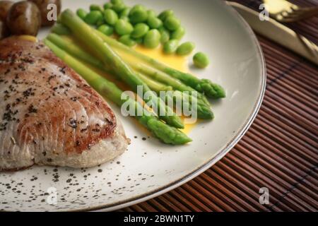 Bistecca di tonno alla griglia servita con asparagi, patate arrosto, fagioli di edamame e salsa hollandaise su un piatto, vista dall'alto Foto Stock