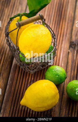 Limoni e lime organici in un cesto su sfondo di legno Foto Stock