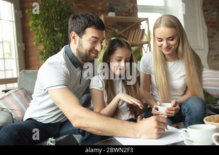 Madre, padre e figlia a casa avendo divertimento, comfort e concetto accogliente. Sembra felice, allegro e gioioso. Bella famiglia caucasica. Trascorrere il tempo insieme, bere tè, giocare. Foto Stock