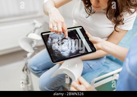Farmaci con una scansione ecografica del feto su un tablet digitale durante un esame con una donna incinta in ufficio, vista ritagliata senza volti Foto Stock