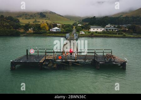 Donna su una giacca rossa in piedi a Port Levy Jetty, Banks Peninsula, Nuova Zelanda Foto Stock