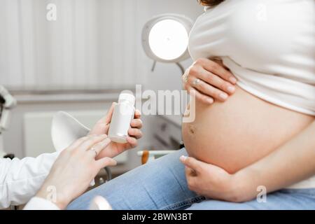 Medico che tiene alcuni farmaci o integratori per una donna incinta durante una consultazione, vista ravvicinata focalizzata sulla pancia incinta. Concetto di farmaco per le donne incinte Foto Stock