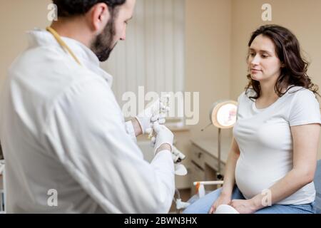 Medico che tiene il vaccino o qualche farmaco nella siringa, che si prepara per l'iniezione per una donna incinta durante una procedura medica in clinica Foto Stock