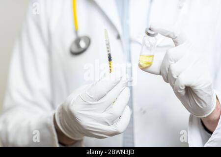 Medico che tiene la siringa con alcuni farmaci o vaccini, vista ravvicinata messa a fuoco sulle mani in guanti medici Foto Stock