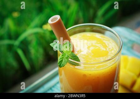 Frullato di mango in vetro con cannucce di bambù su tavolo di legno all'aperto, guardaroba Foto Stock