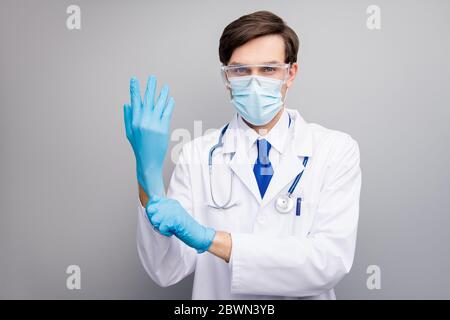 Foto di bel ragazzo serio dottore specialista chirurgo professionale preparazione operazione indossare guanti facciale maschera protettiva medica uniforme camice da laboratorio Foto Stock