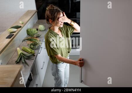 Giovane donna che guarda nel frigorifero, sentendosi affamato di notte. Concetto di mangiare e mangiare troppo spesso di notte Foto Stock