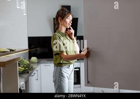 Giovane donna che guarda nel frigorifero, sentendosi affamato di notte Foto Stock