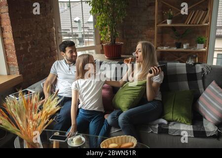 Madre, padre e figlia a casa avendo divertimento, comfort e concetto accogliente. Sembra felice, allegro e gioioso. Bella famiglia caucasica. Trascorrere il tempo insieme, bere tè, mangiare croissant, icecream. Foto Stock