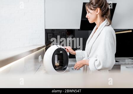 Giovane donna in accappatoio che fa caffè con una macchina da caffè in cucina a casa Foto Stock