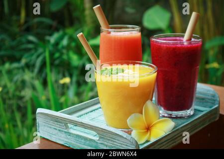 Frullati di frutta, papaya e mango in bicchieri con cannucce di bambù e frutta tropicale fresca all'aperto Foto Stock