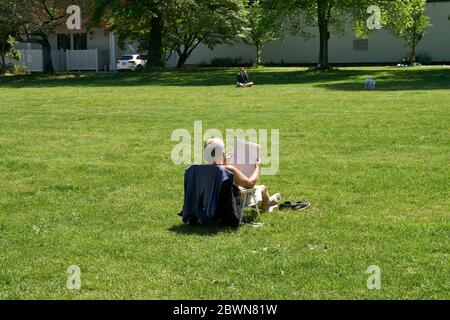 Un anziano seduto da solo sull'erba in un parco mentre legge un giornale, Vancouver, BC, Canada Foto Stock