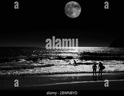 Surfers di notte sulla spiaggia di Dun Cin Tire illuminata da una luna super, vicino a Dingle Town, Dingle Peninsula, County Kerry, Irlanda Foto Stock