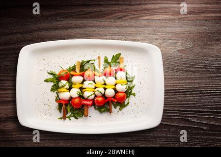 Direttamente sopra un colpo di spiedini di pomodoro, pepe e mozzarella su un letto di razzo vestito servito in un piatto Foto Stock