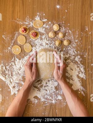 Mani da uomo che tengono una palla di impasto. Preparazione di gnocchi di carne sul tavolo di legno. Foto Stock