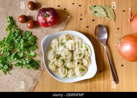 Ciotola di gustosi gnocchi in brodo, servita su tavola di legno, con verdure fresche intorno. Vista dall'alto. Foto Stock