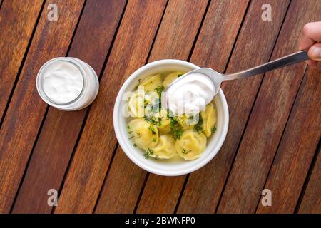 Ciotola di gustosi gnocchi in brodo, servita su tavola di legno, con panna acida. Vista dall'alto. Foto Stock