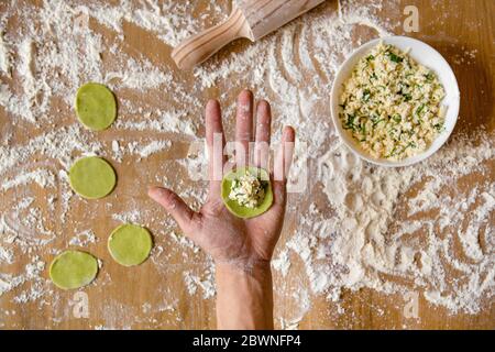 Mani da uomo che tengono un vuoto per gnocchi vegetali. Preparazione di gnocchi di carne sul tavolo di legno. Foto Stock