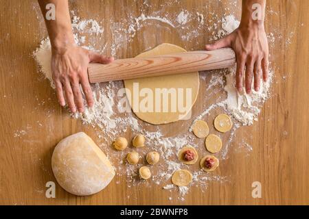 Pasta da arrotolare per le mani degli uomini per la preparazione di gnocchi di carne sul tavolo di legno. Foto Stock
