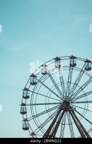 Una vista distante di una ruota panoramica vintage in una zona fieristica sul mare con spazio per la copia e sfondo blu Foto Stock