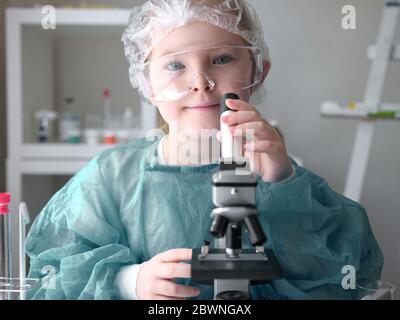 Carina bambina che guarda al microscopio a casa sua. Giovane scienziato che fa esperimenti nel suo laboratorio domestico. Concetto di istruzione. Foto Stock