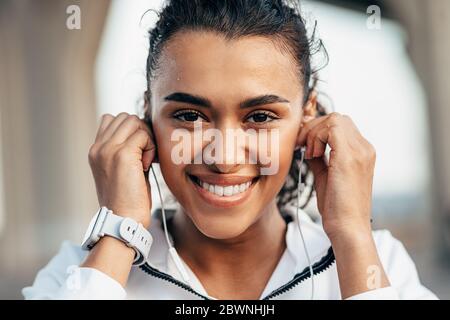 Primo piano ritratto di una bella donna che guarda la fotocamera e tiene gli auricolari Foto Stock