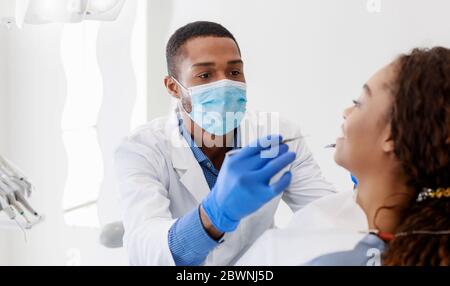 Stomatologo uomo nero che controlla i denti della giovane donna in clinica, panorama Foto Stock