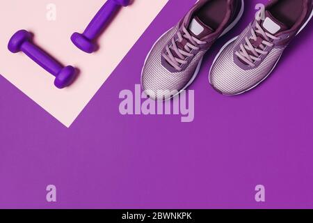 Manubri e sneaker per l'allenamento domestico su sfondo viola. Foto Stock