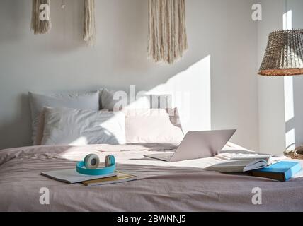Interni moderni e accoglienti con camera da letto con computer portatile, cuffie, libri su un comodo letto. Foto Stock