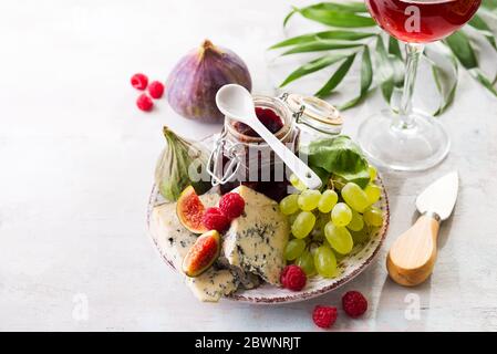 Assortimento di formaggi, bacche e uve con vino rosso in calici. Su fondo di pietra. Spazio di copia Foto Stock