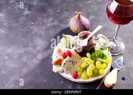 Assortimento di formaggi, bacche e uve con vino rosso in calici. Su fondo di pietra. Spazio di copia Foto Stock