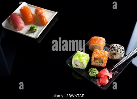 Grandi set di sushi con un sacco di sushi, roll. Elegante sushi si fissa su un piano e tavolo in ceramica nera con bastoncini cinesi. Spazio di copia Foto Stock